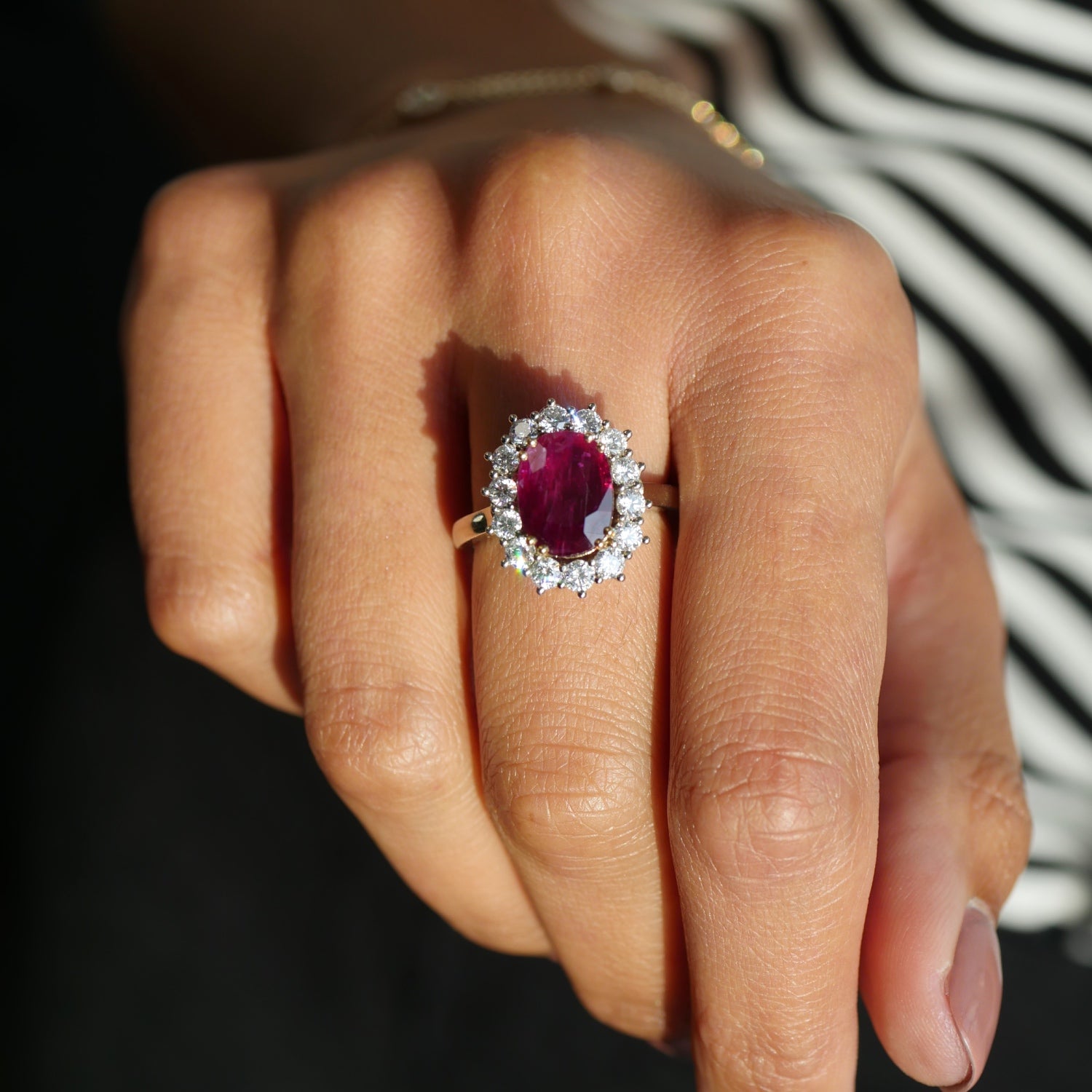 Oval-Shaped Ruby and Round Brilliant Cut Diamond Cluster Ring on a Hand