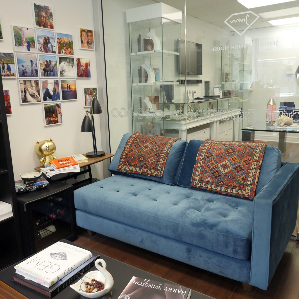 Blue sofa with patterned cushions beside glass jewelry displays and a wall of photographs at the Jewelry Design House atelier in Montreal.