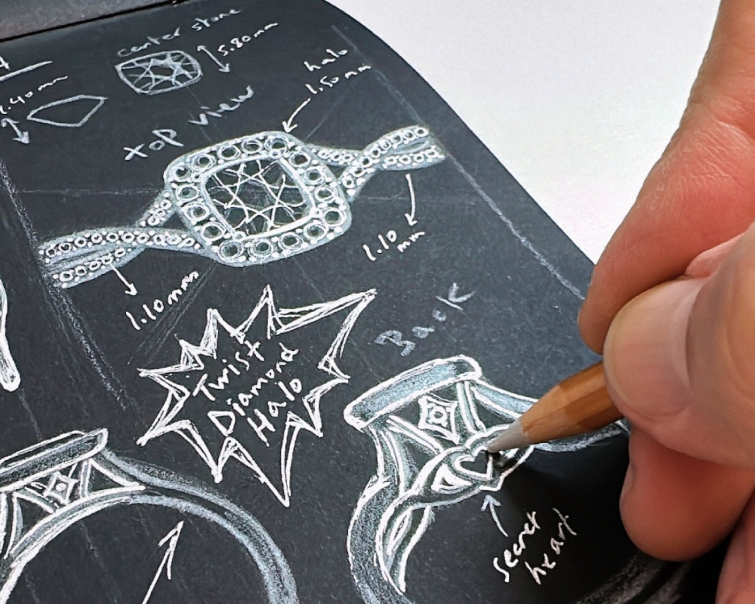 Hand sketching a custom diamond engagement ring with design details and measurements on dark paper.