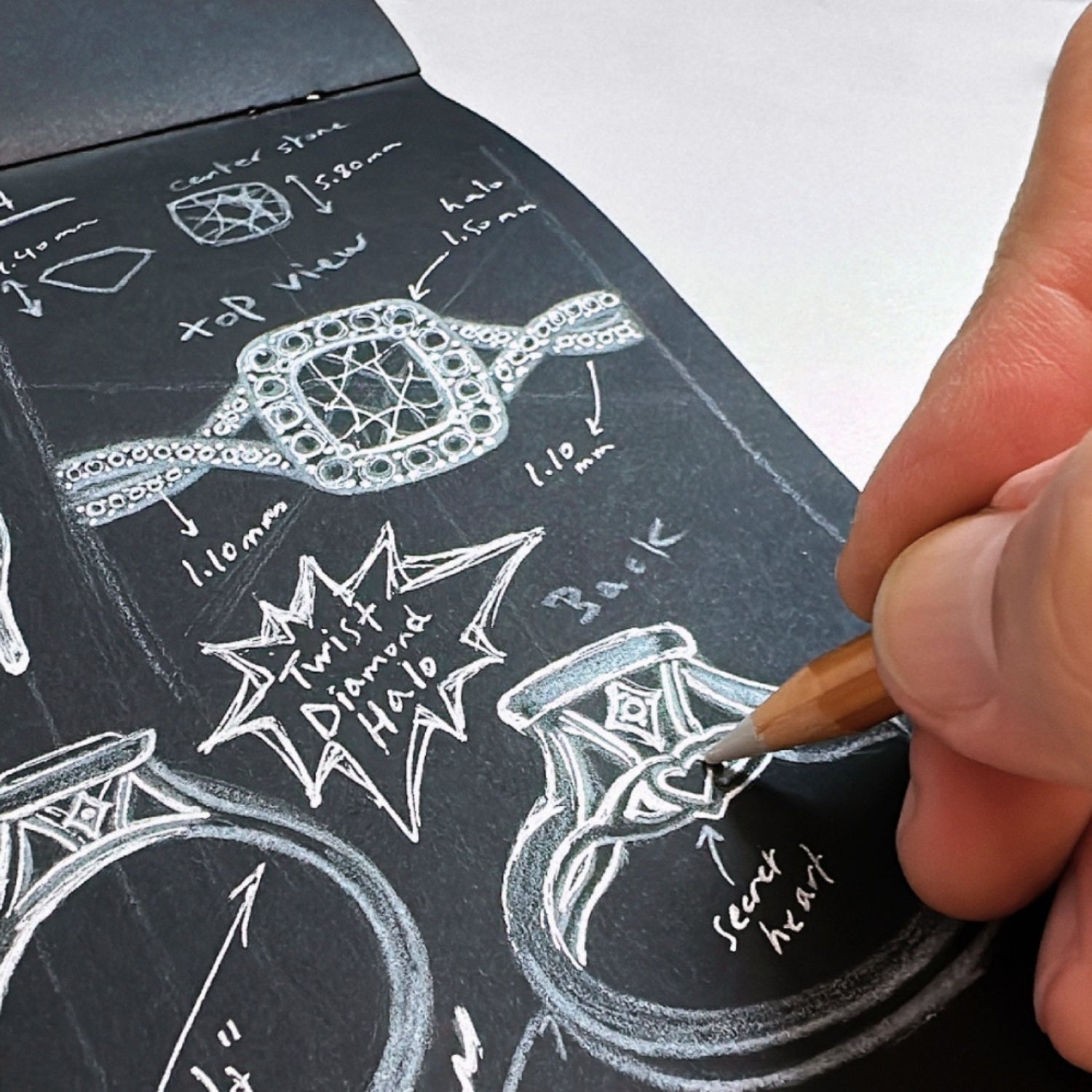 Hand sketching a custom diamond engagement ring with design details and measurements on dark paper.