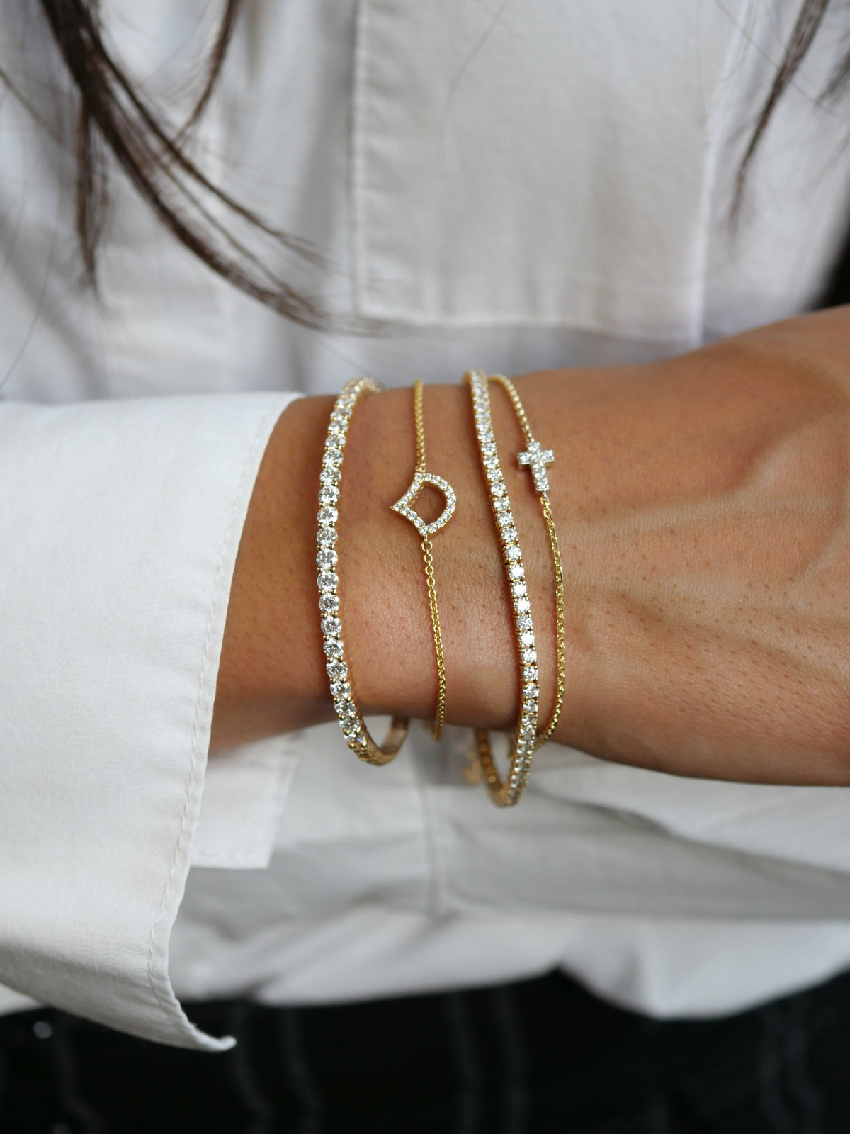Diamond tennis bracelets and delicate gold bracelets with pavé motifs worn together on a wrist.