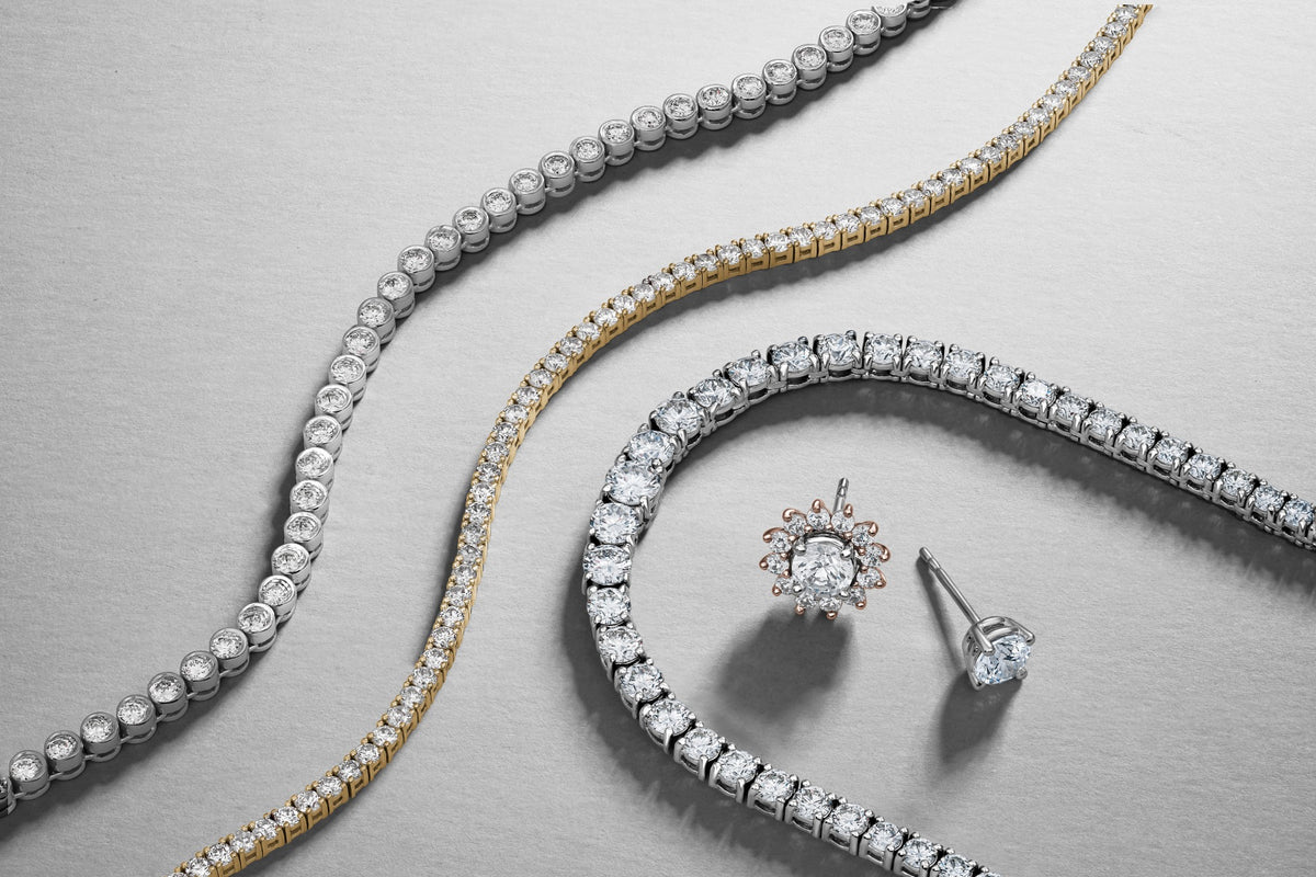 Diamond tennis bracelets and stud earrings arranged on a grey background.