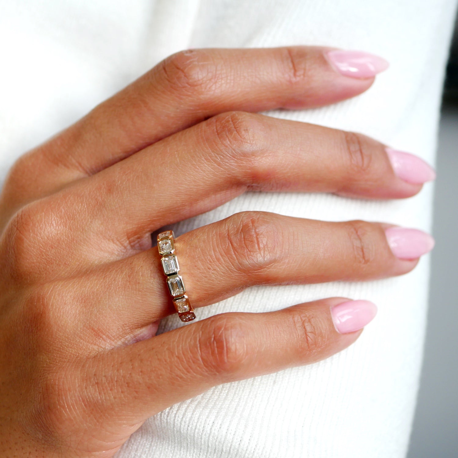 Emerald-cut lab-grown diamond bezel half-eternity ring in yellow gold, worn on a hand.