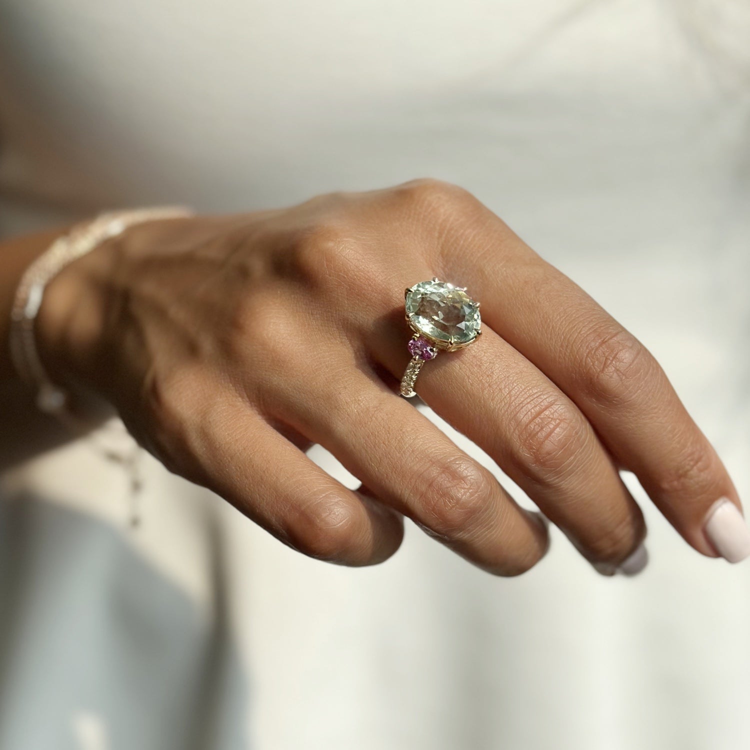Yellow gold Mermaid ring featuring an oval aquamarine flanked by pink sapphires and a diamond pavé band, worn on the hand