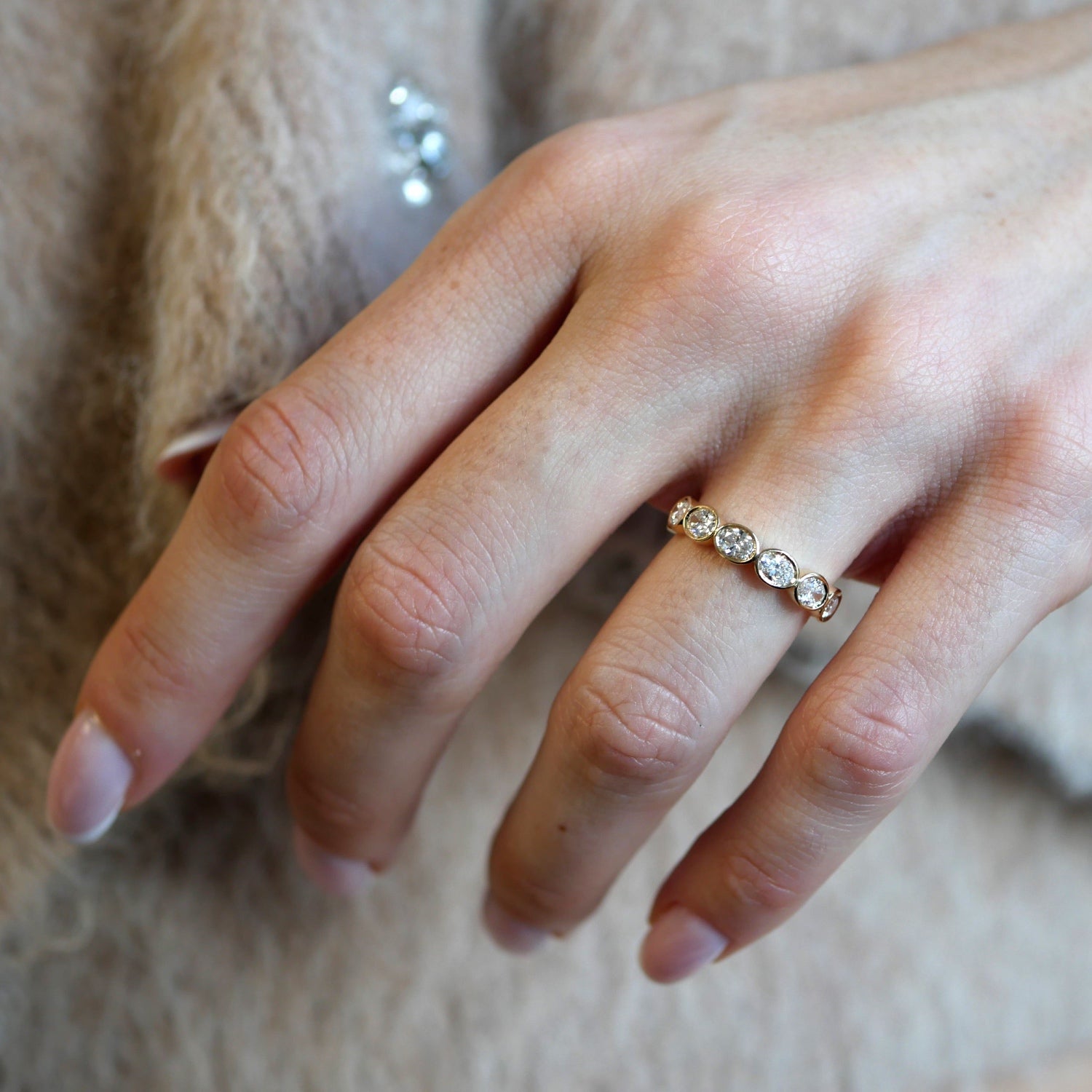 Oval-shaped lab-grown diamond bezel half-eternity ring in yellow gold, worn on a hand.