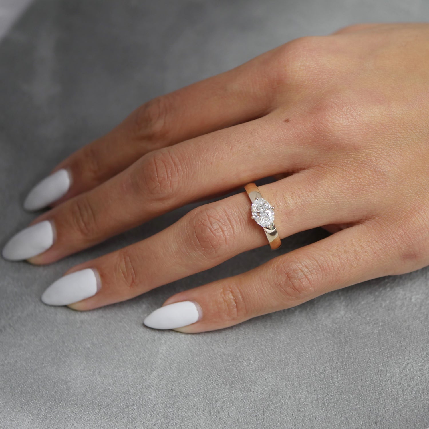 Oval-shaped lab-grown diamond east-west engagement ring in yellow gold with a wide polished band, worn on a hand.