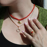 Coral bead necklace with a freshwater pearl set in a gold seashell pendant, worn around the neck.