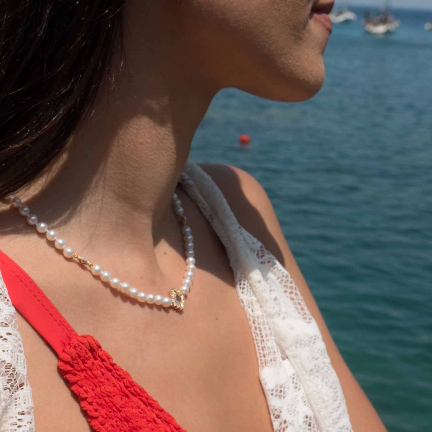 Woman wearing a pearl necklace by Jewelry Design House beside the sea.