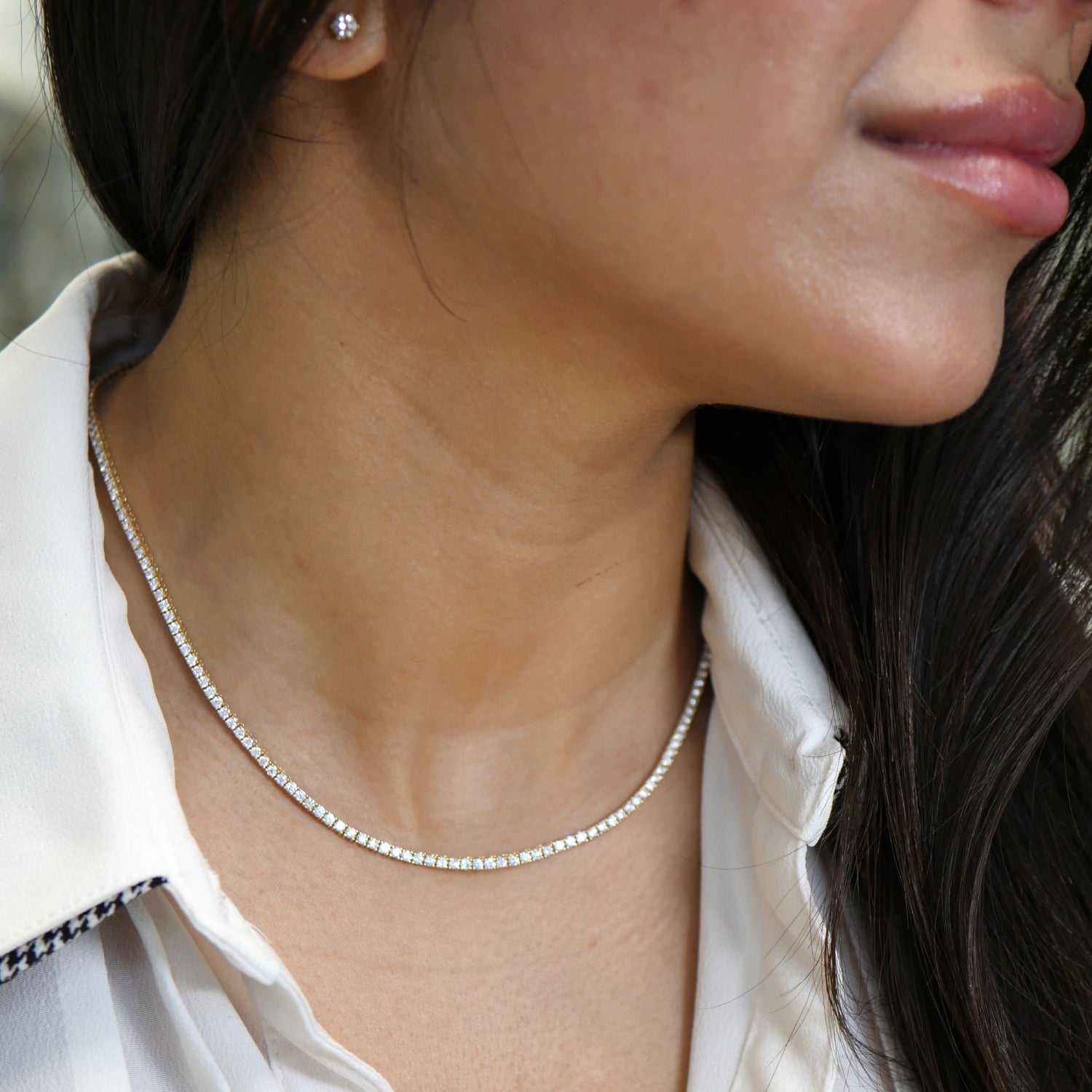Round brilliant cut diamond tennis necklace worn around the neck.