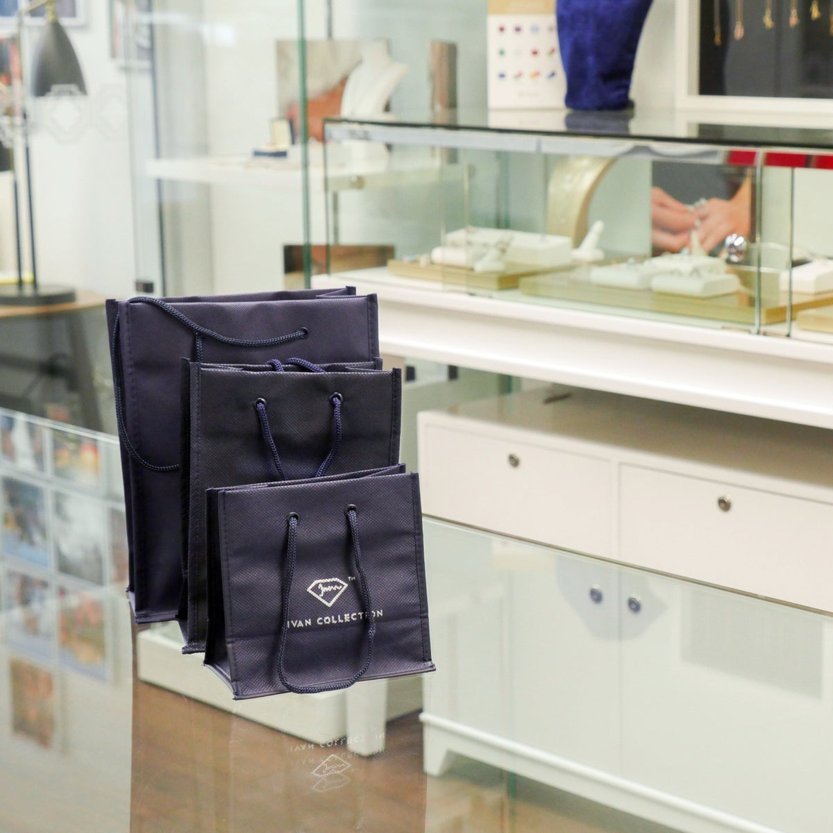 Three navy Jivan Collection shopping bags on a glass counter at the Jewelry Design House atelier in Montreal.