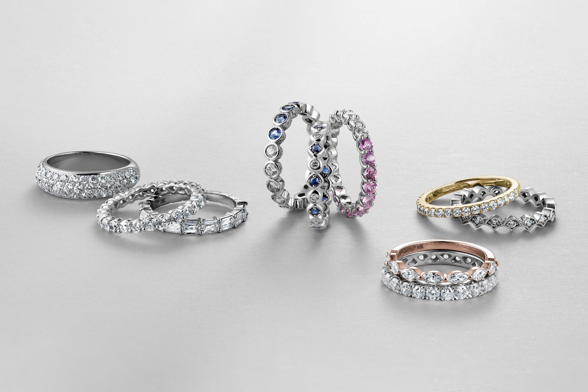 Women’s diamond and coloured gemstone wedding bands arranged in groups on a light grey background.