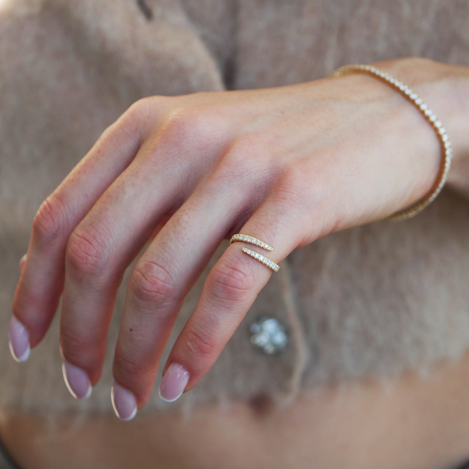 Wrap-around diamond pavé pinky ring in yellow gold, worn on a hand alongside a diamond tennis bracelet.